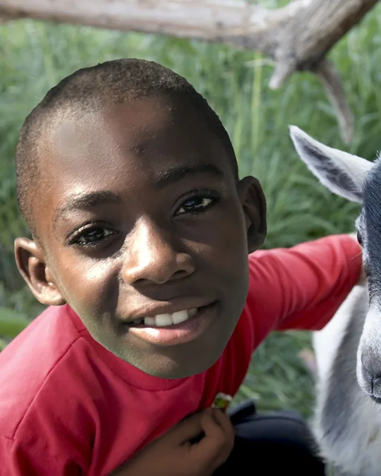 A smiling student with one of the school goats